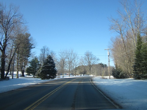 A empty rural road with snow on roadside, utility poles line the street