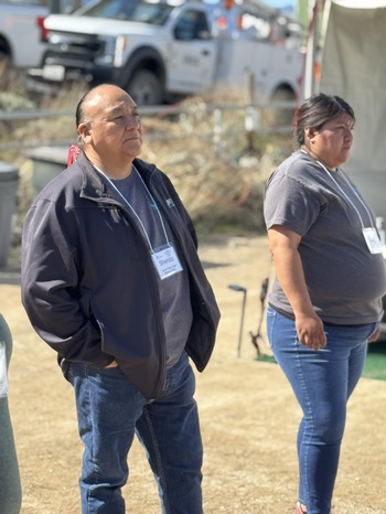 Kevin Shendo JNET director stands looking at on off camera demo with his hands in jeans pockets standing next to a JNET technician in training with a utility truck in the background