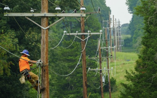A utility worker is suspended on utility pole deploying aerial fiber strands in a rural area