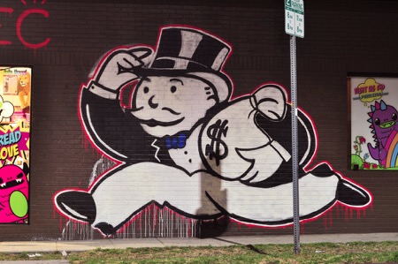 Street art on side of building depicts Mr. Monopoly running off with a bag of cash