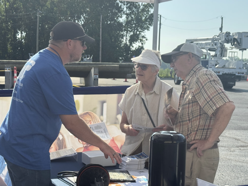 A Paulding Putnam Electric Cooperative speaks with an elderly couple about the co-ops new fiber Internet offering at a table outside