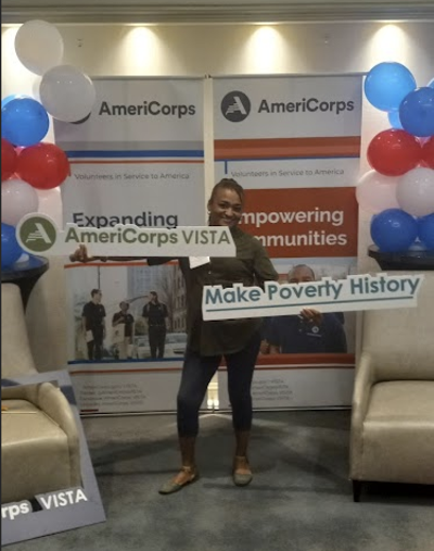 Belinda Parker-Mendoza at digital skills event holding two signs. One says: "Americorps VISTA," the other reads: "Make Poverty History"