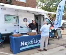 Nextlight rep standing behind a table in front company truck at street fair talking to an elderly gentleman