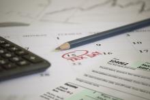 A calculator and tax form lay across a calendar with tax day (April 15) circled