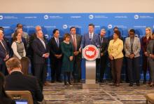 Two dozen mayors stand behind podium at US Conference of Mayors Summit 2025 
